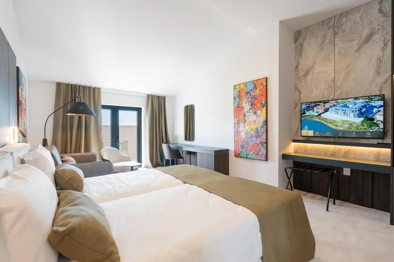 Une chambre lumineuse avec un grand lit et un tableau coloré au-dessus d'un meuble bas.