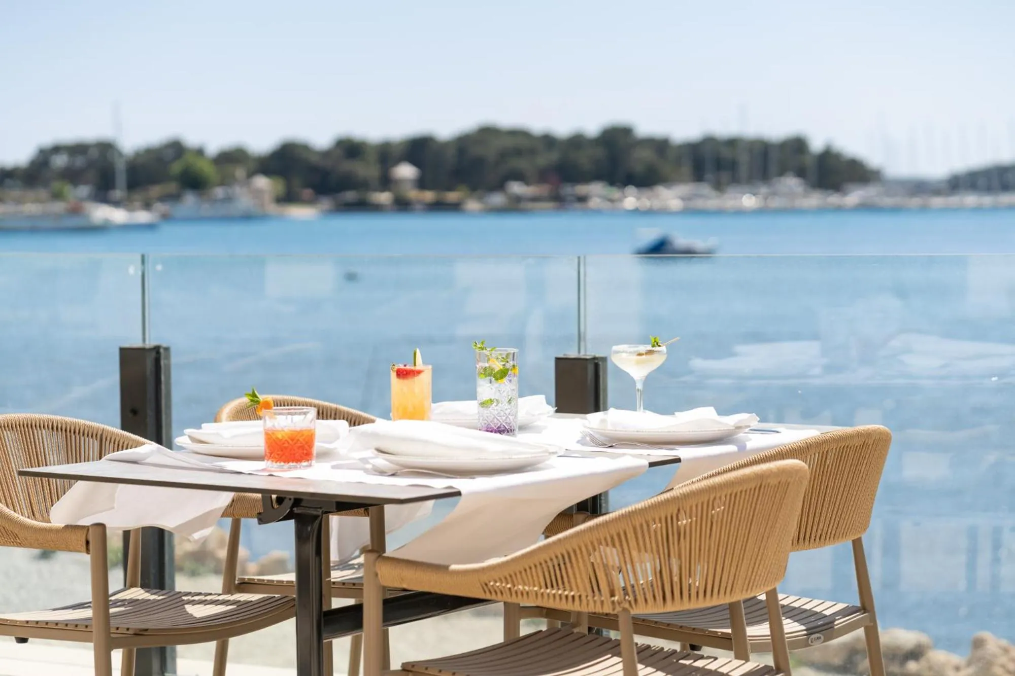 Une table dressée avec des boissons colorées en terrasse face à la mer.