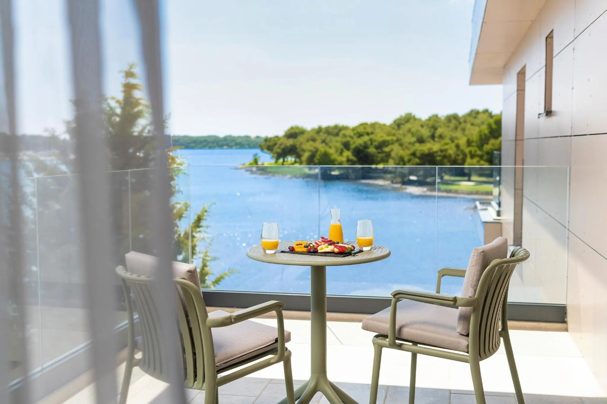 Une table avec des boissons et des fruits est mise en scène sur une terrasse avec vue sur la mer.