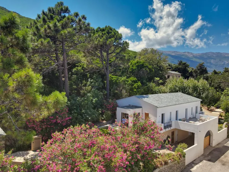 Vue aérienne d'une maison blanche entourée de végétation luxuriante et de montagnes.