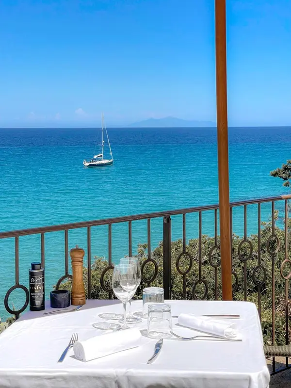 Table dressée sur une terrasse avec vue sur la mer et un voilier.