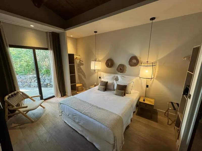 Une chambre lumineuse avec un lit double et un fauteuil en osier.