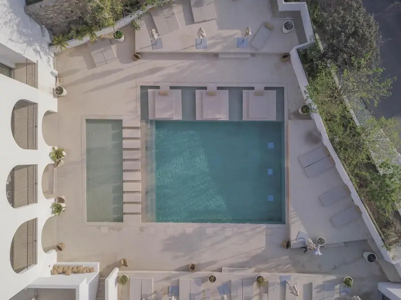 Vue aérienne d'une piscine rectangulaire entourée d'une terrasse blanche.