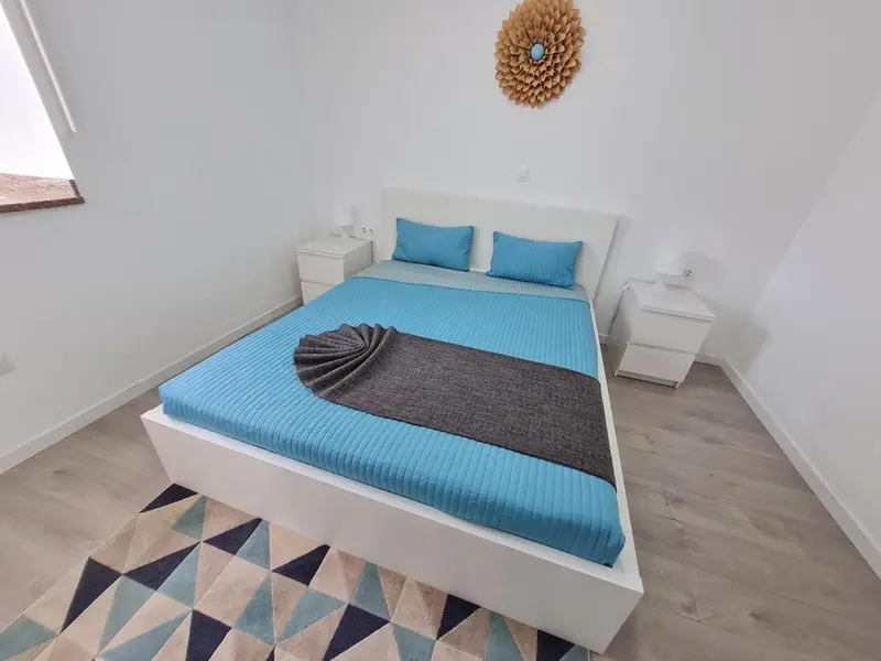 Une chambre lumineuse avec un grand lit recouvert d'une courtepointe bleue.