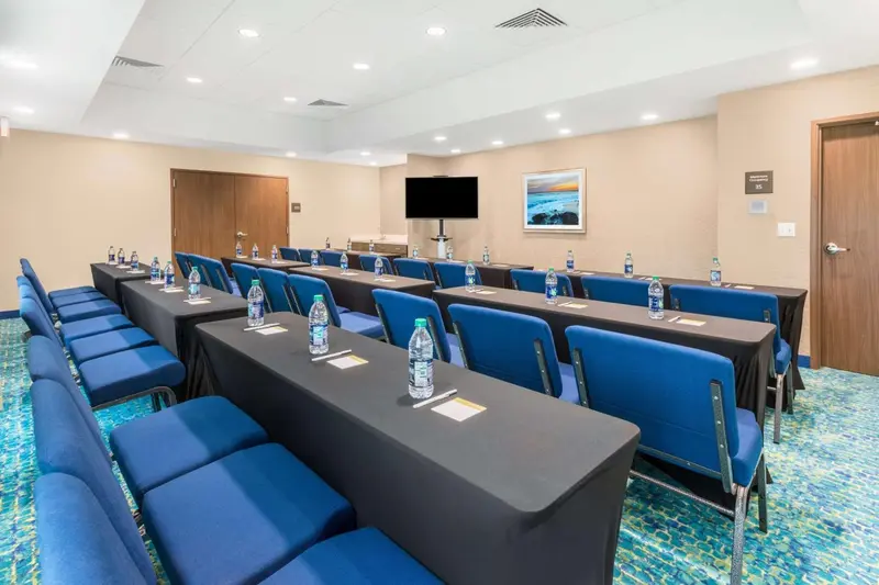 Une salle de réunion avec des tables et des chaises alignées, ainsi que des bouteilles d'eau sur chaque place.