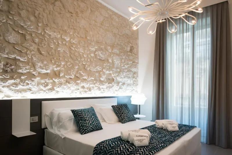 Une chambre lumineuse avec un mur en pierre et un lit recouvert d'une courtepointe à motifs.
