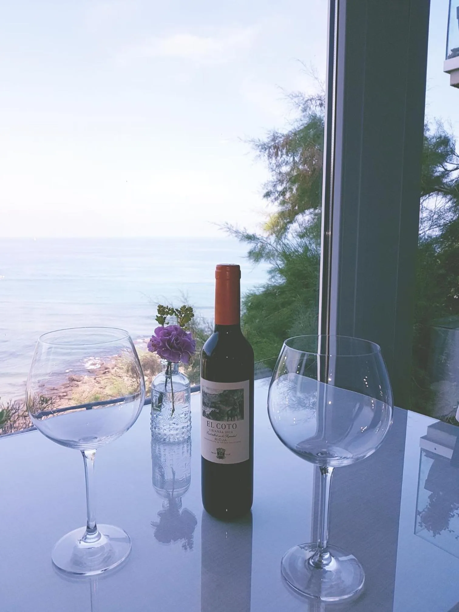 Une table est mise avec deux verres à vin et une bouteille devant une vue sur la mer.