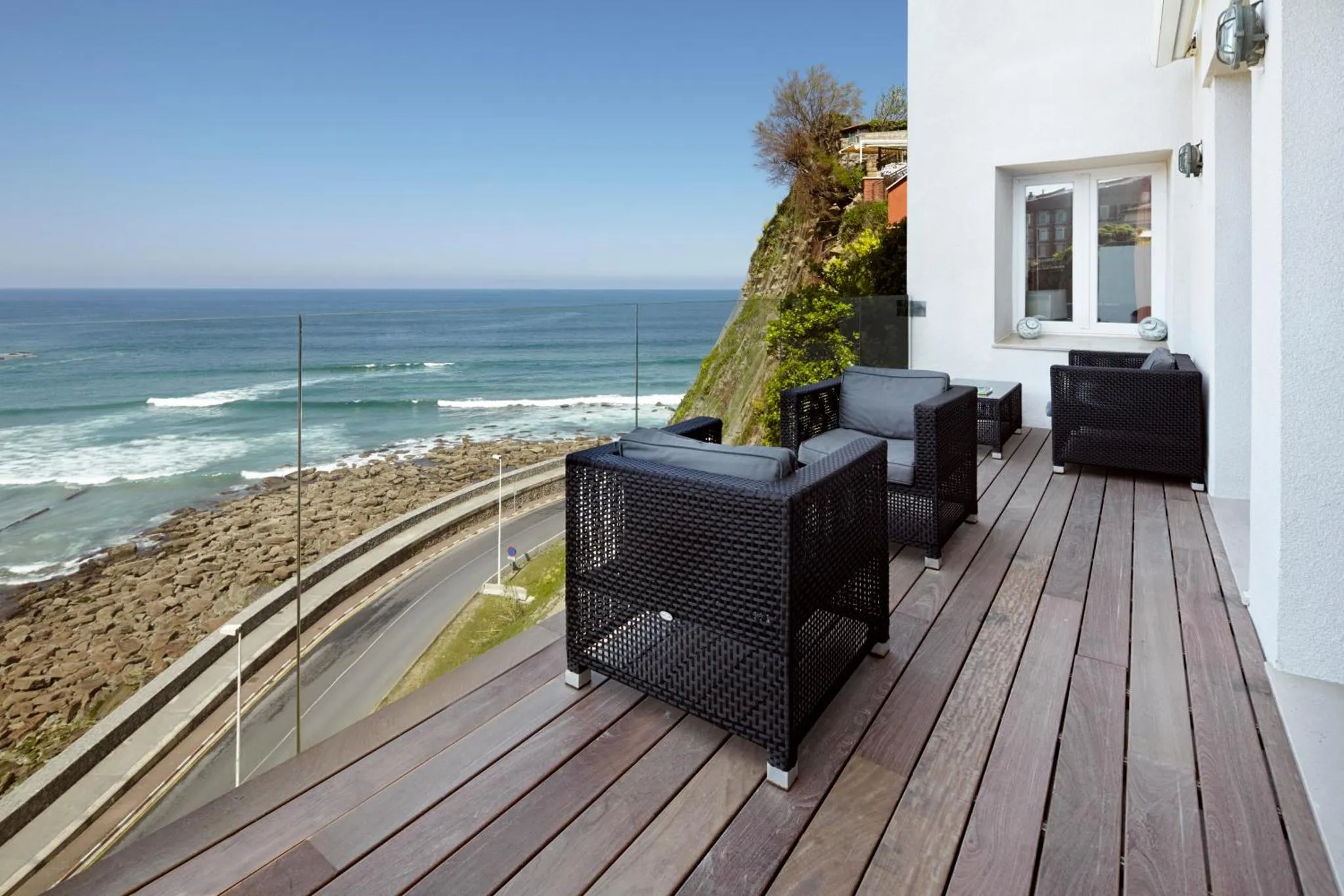 Terrasse en bois avec mobilier noir donnant sur la mer et la côte rocheuse.