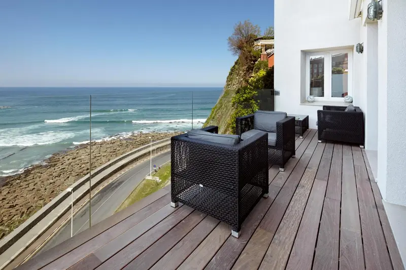 Terrasse en bois avec mobilier noir donnant sur la mer et la côte rocheuse.