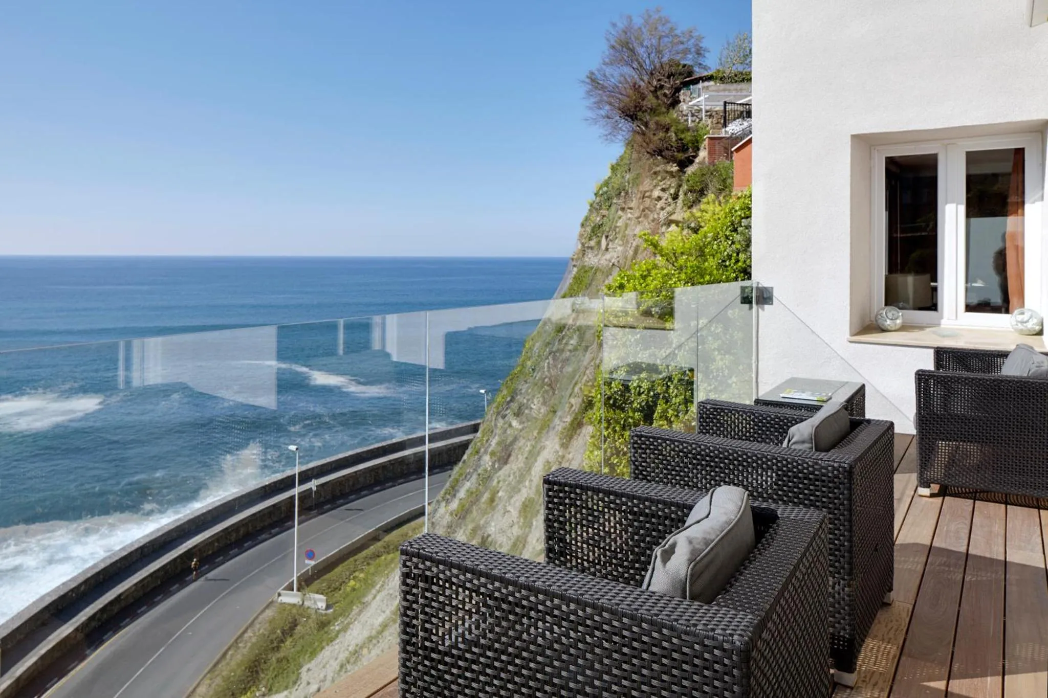 Terrasse avec mobilier en rotin donnant sur la mer et une route côtière.