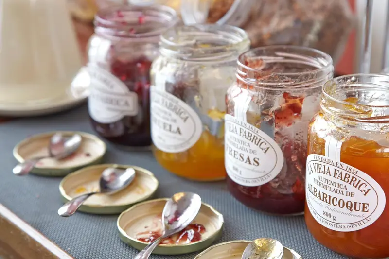 Des pots de confiture artisanale variés sont présentés sur une table avec de petites cuillères.