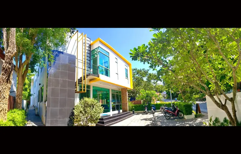 Façade moderne d'un bâtiment blanc et jaune entouré de végétation tropicale.