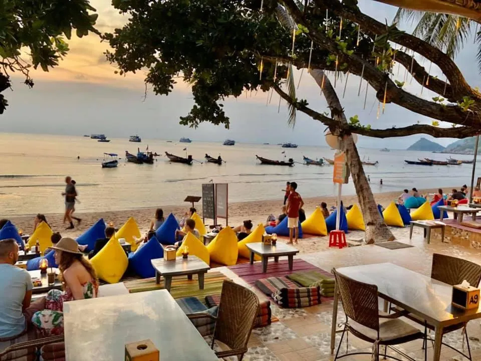 Une terrasse de bar animée face à la mer au coucher du soleil.