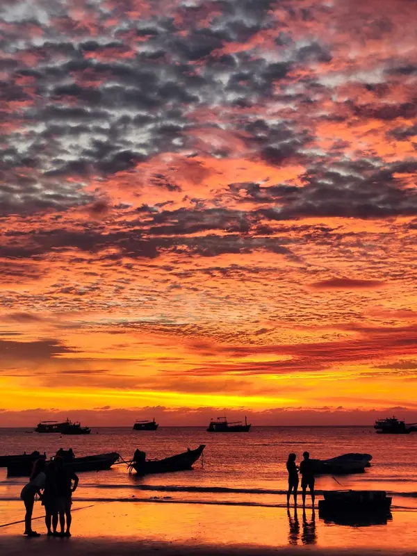 Coucher de soleil flamboyant sur l'océan avec des silhouettes sur la plage.