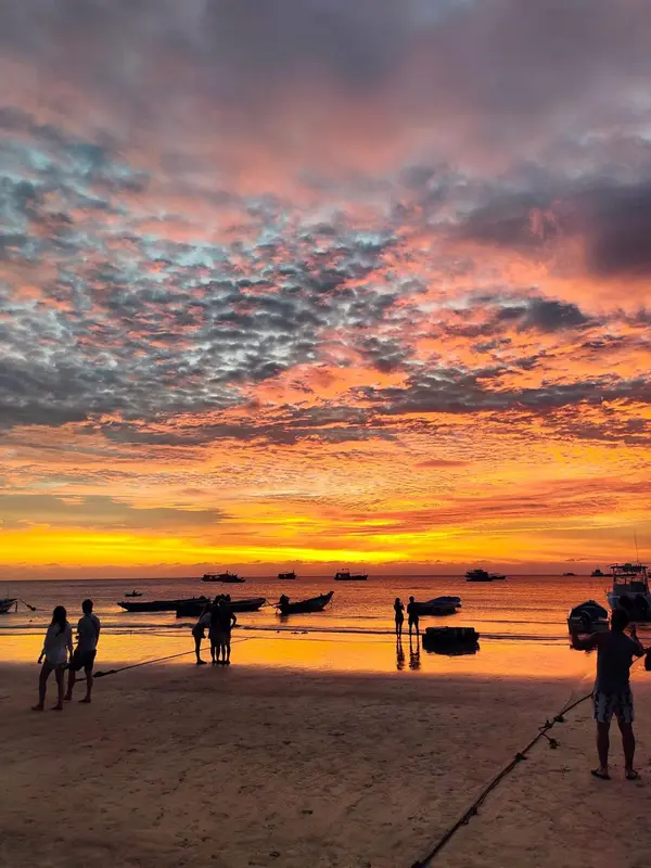 Une plage au coucher du soleil avec des bateaux à l'horizon.