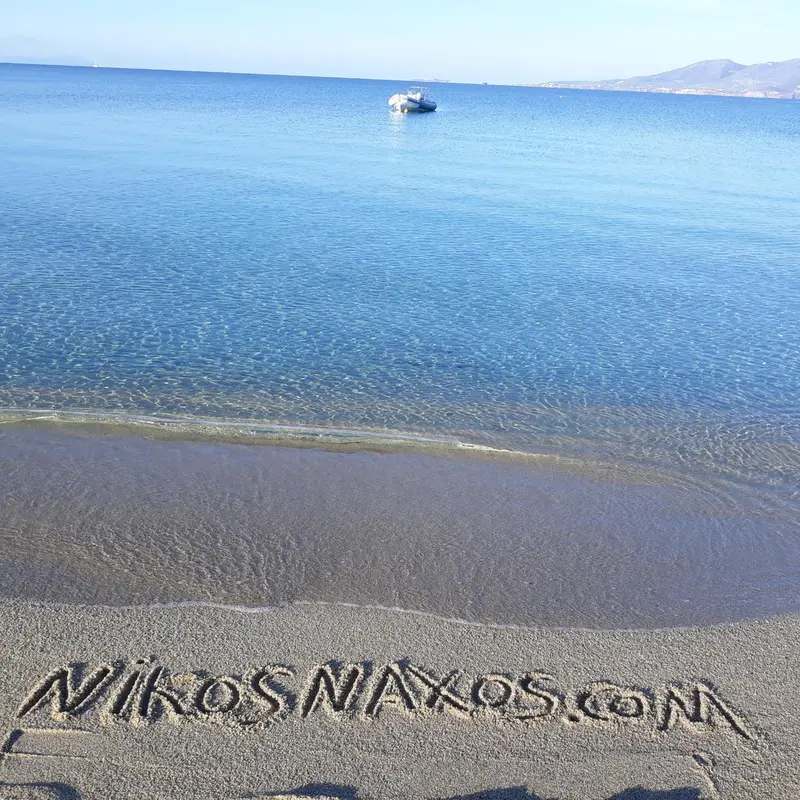 Plage de sable sombre avec une mer bleue et des montagnes en arrière-plan.