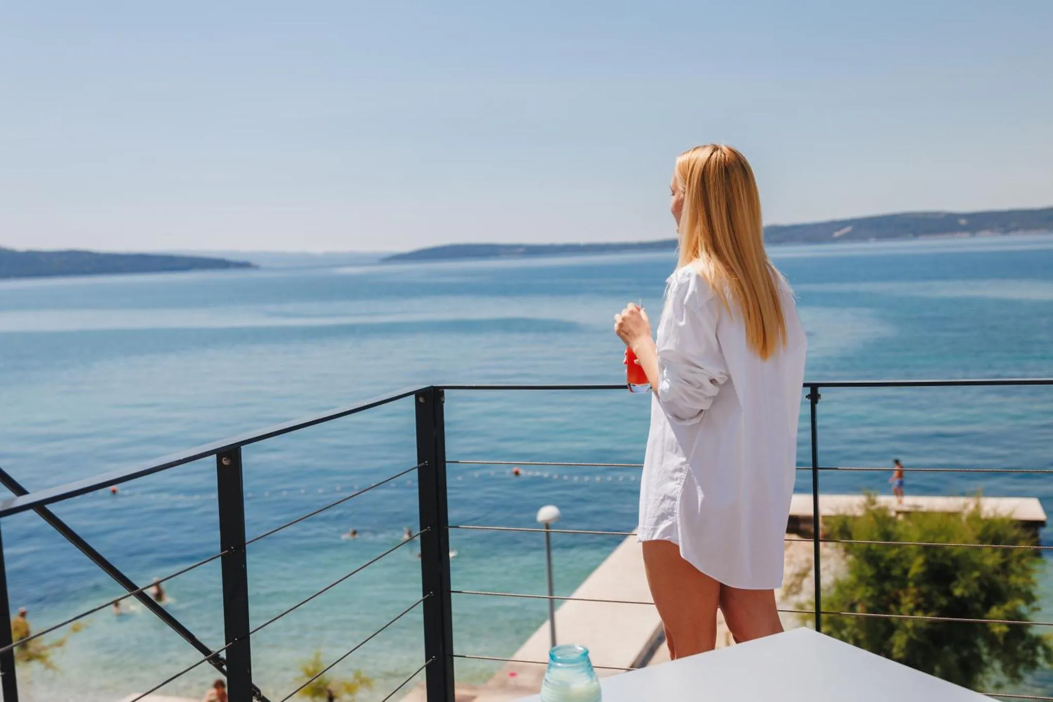 Une femme regarde la mer depuis une terrasse ensoleillée.
