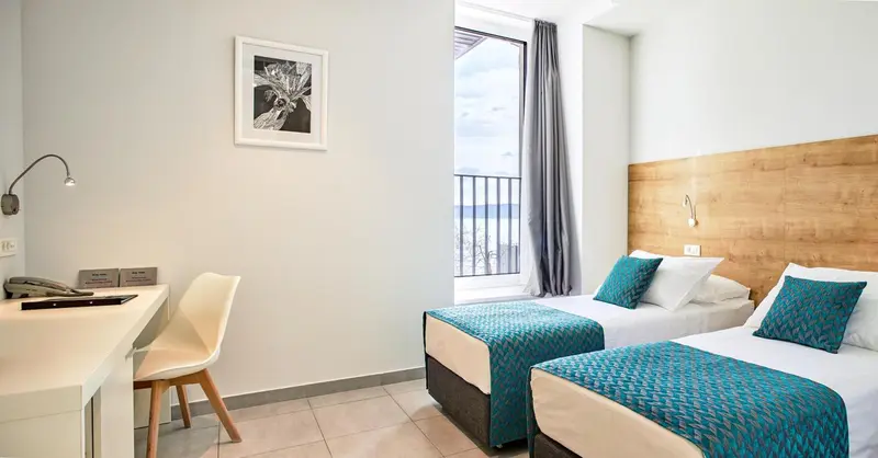 Une chambre lumineuse avec deux lits simples et un bureau près d'une fenêtre.