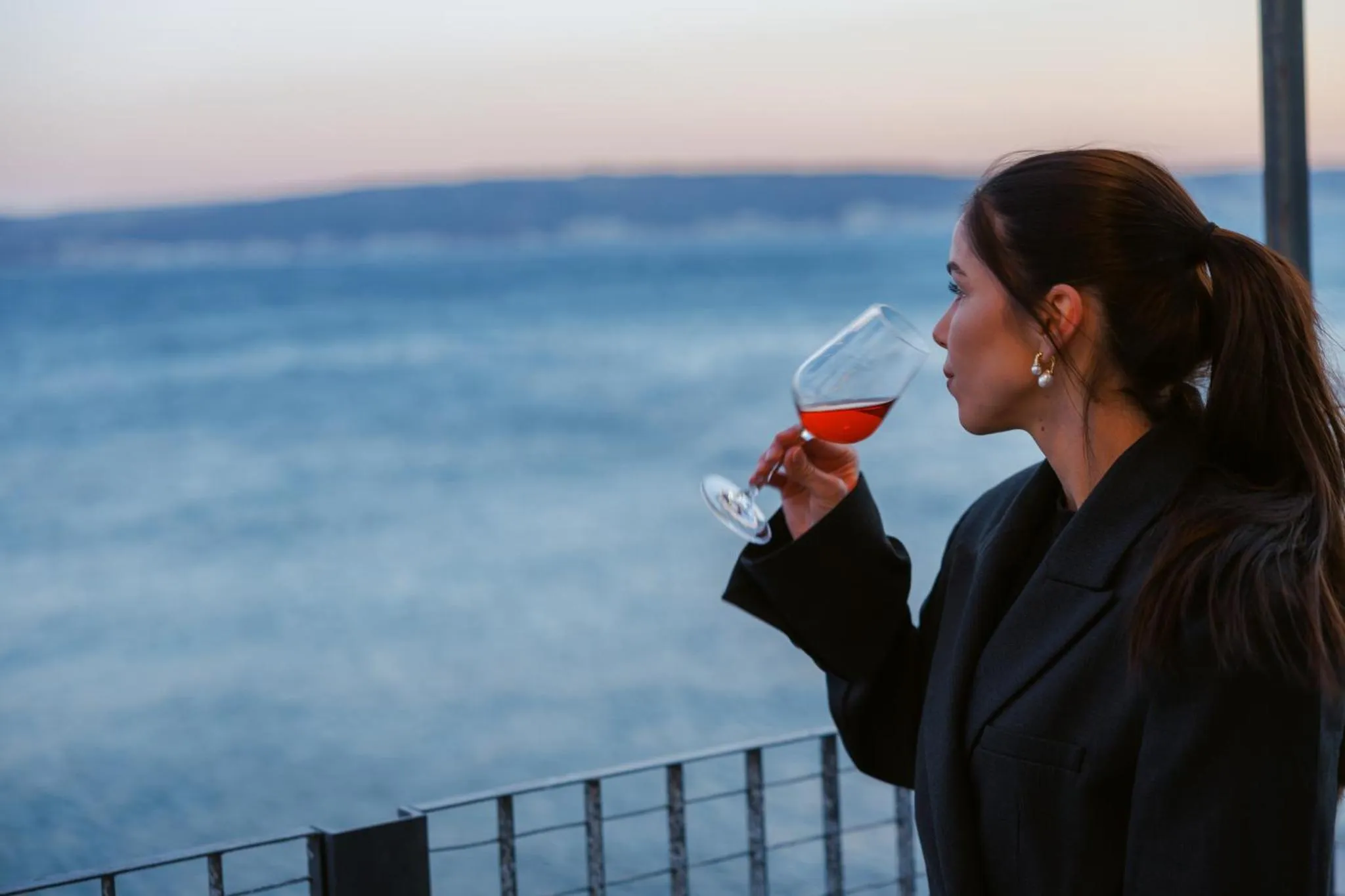 Une personne admire la vue sur la mer en tenant un verre.