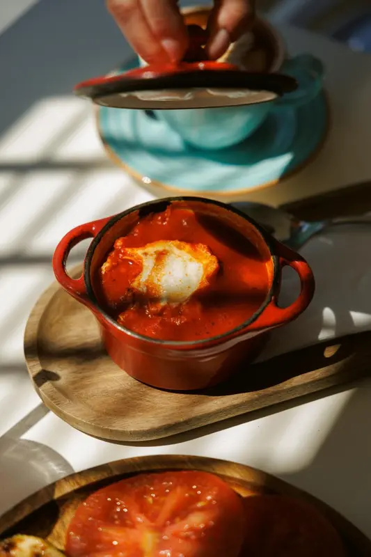 Un plat de cuisine rouge avec un œuf poché est présenté sur une planche en bois.