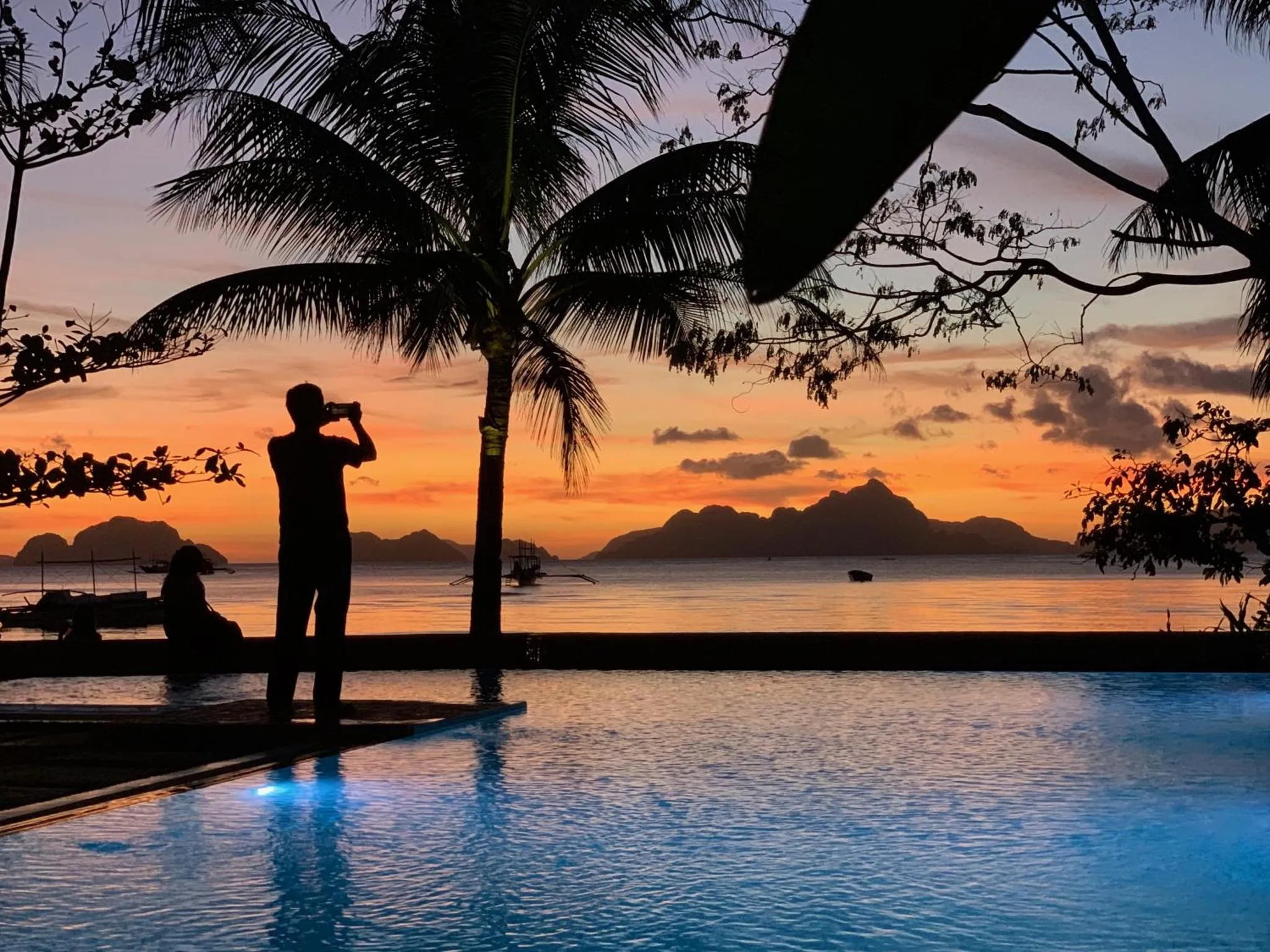 Une personne prend une photo au bord d'une piscine au coucher du soleil.