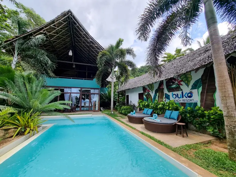 Une piscine turquoise bordée de chaises longues dans un jardin tropical.