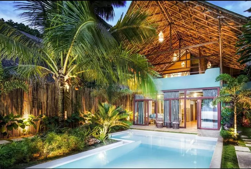 Une piscine privée devant une structure en bois et bambou éclairée.