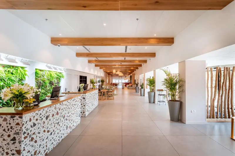 Un long couloir mène à un comptoir d'accueil décoré de motifs clairs et de plantes.