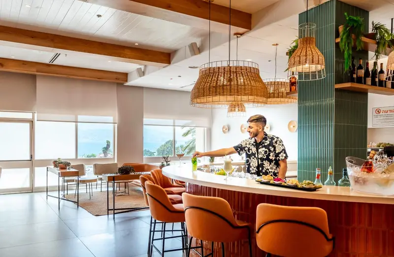 Un barman prépare un cocktail devant un comptoir orange et des tabourets hauts.