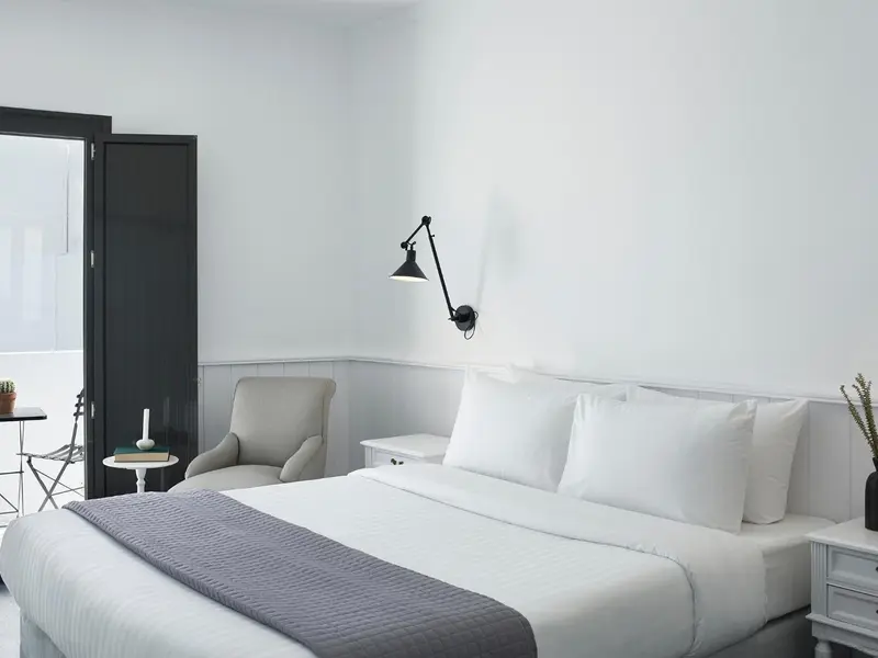Une chambre lumineuse avec un lit fait et un fauteuil.