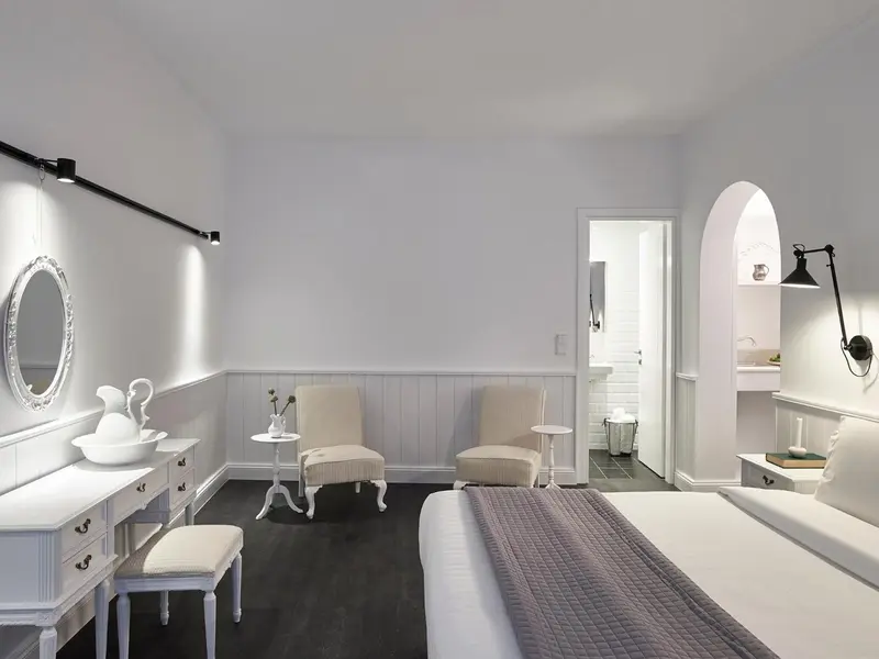 Une chambre lumineuse avec un lit recouvert d'une couverture grise et un coin salon.