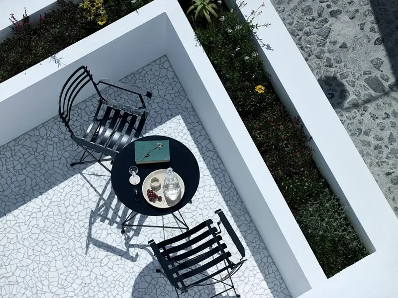 Une table ronde avec des verres et des fruits est entourée de deux chaises sur une terrasse carrelée.