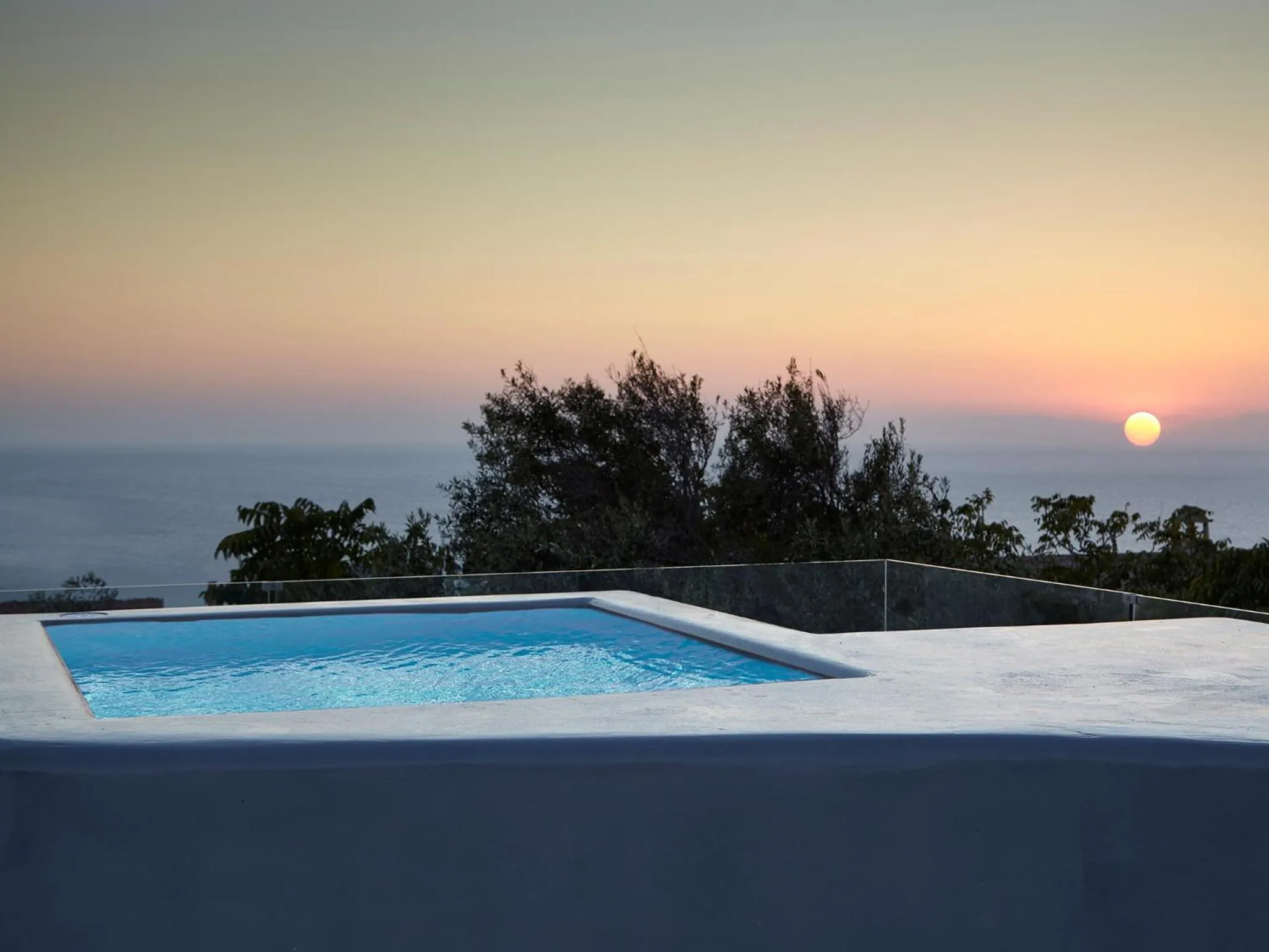 Une piscine à débordement offre une vue sur la mer au coucher du soleil.