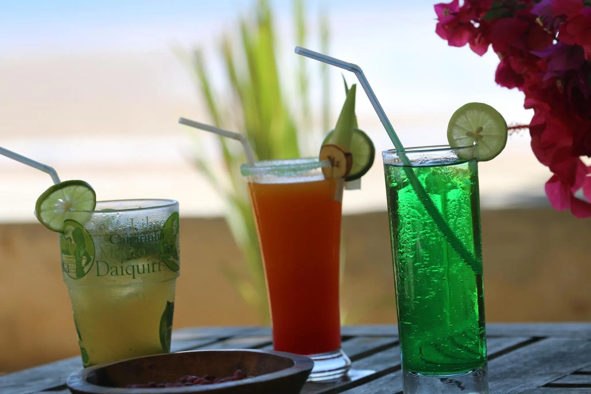 Trois verres colorés garnis de tranches de citron vert sur une table en bois.