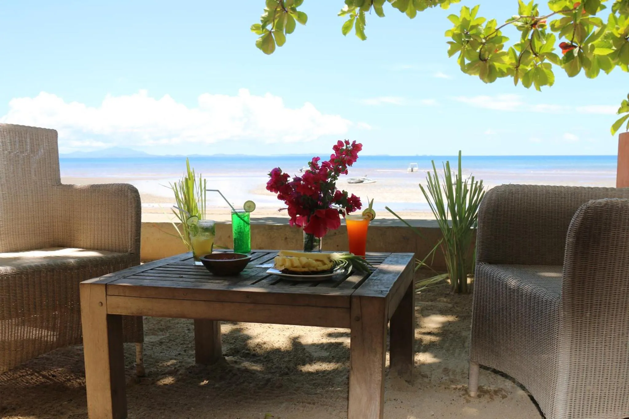 Une table basse avec des boissons et des fruits est placée entre deux fauteuils en osier face à la mer.