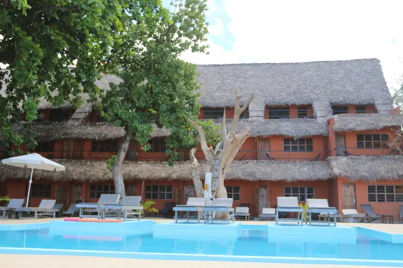Bâtiment à toits de chaume surplombant une piscine et des transats.