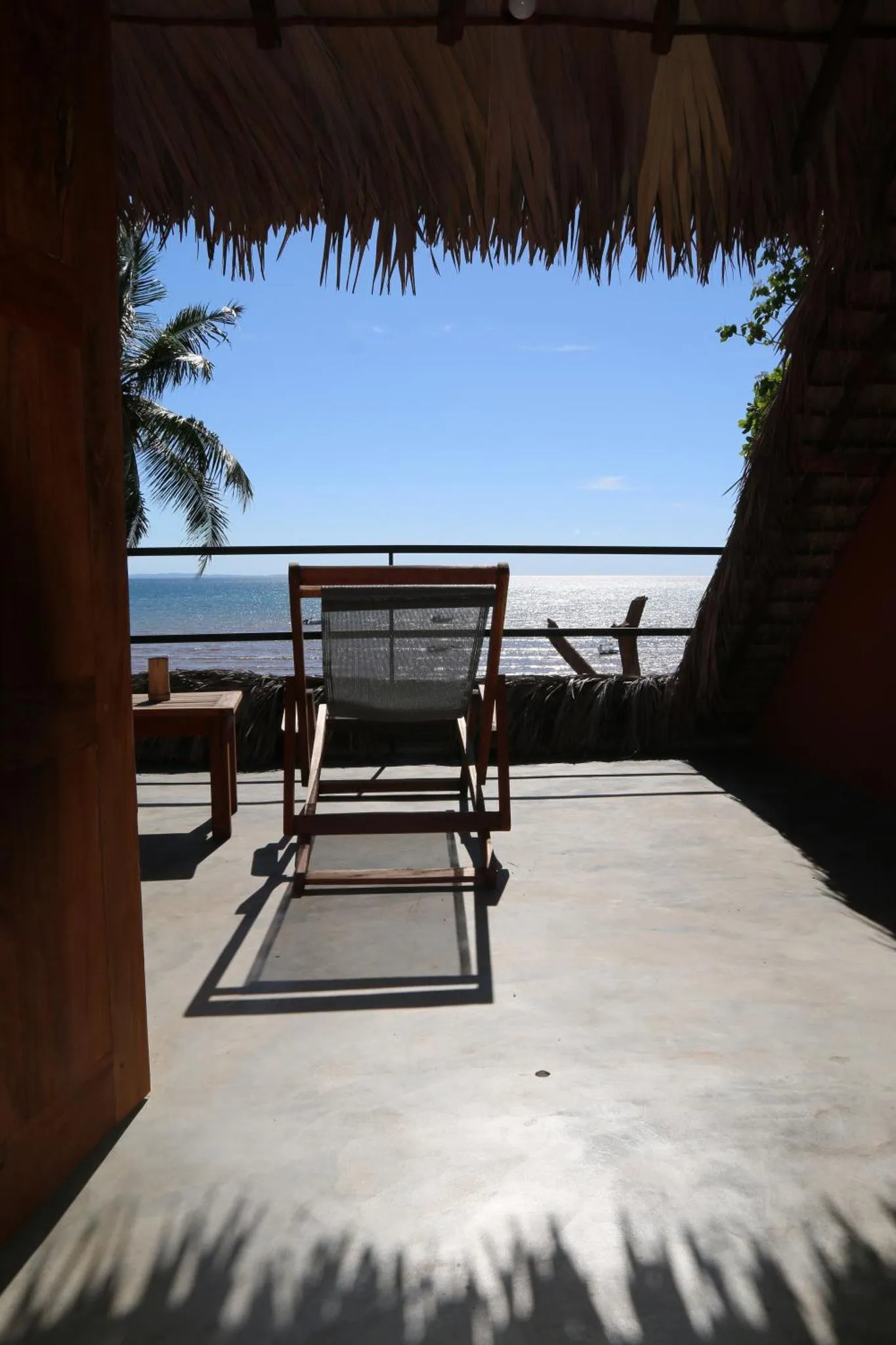 Une chaise longue se trouve sur une terrasse ombragée face à la mer.