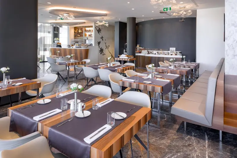 Une salle de restaurant lumineuse avec des tables dressées et un comptoir de boissons.