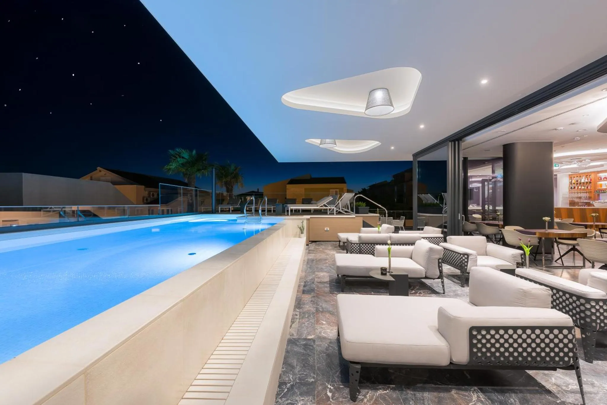 Terrasse avec piscine illuminée et mobilier de détente.