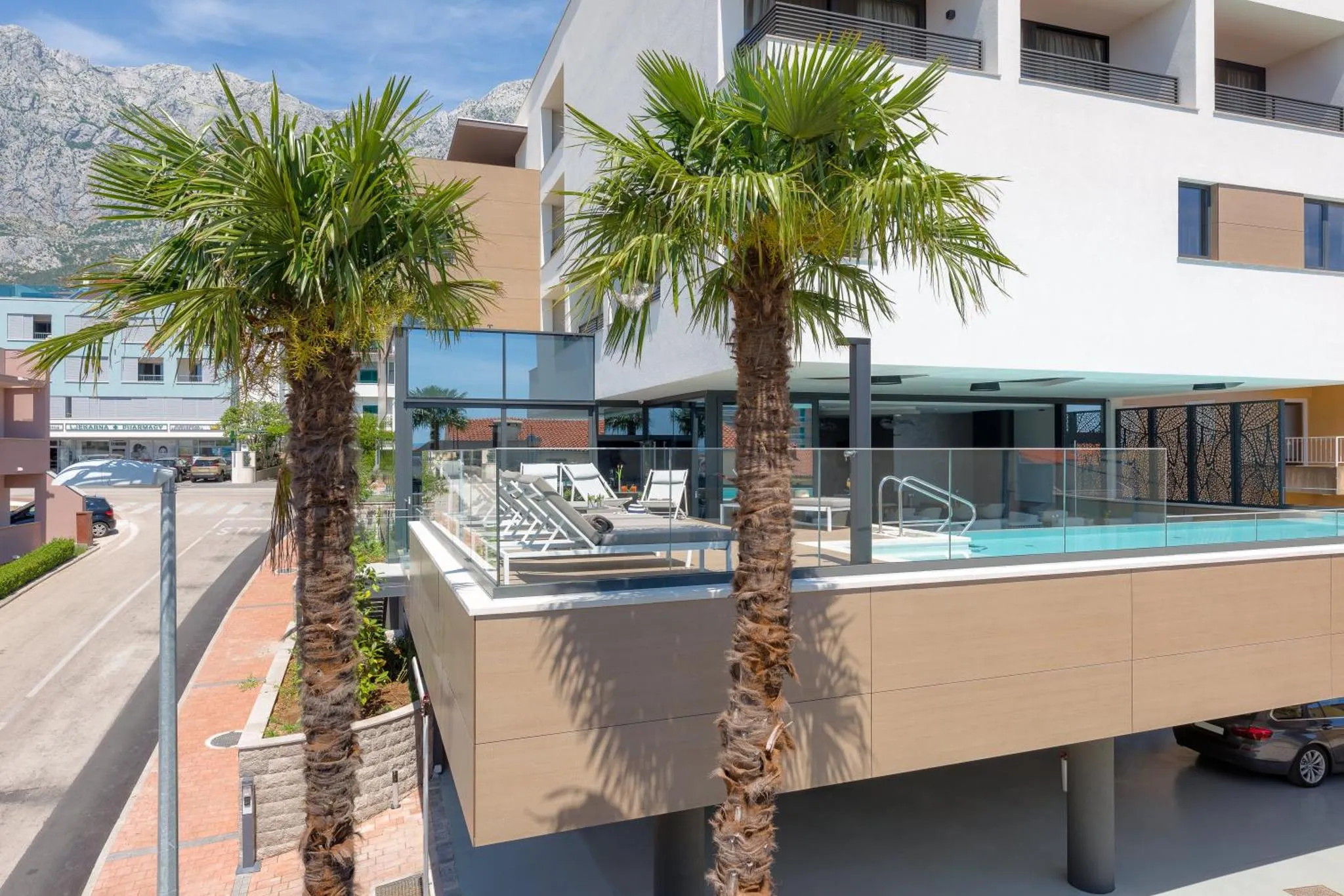 Vue d'une piscine avec transats et palmiers devant un bâtiment moderne.