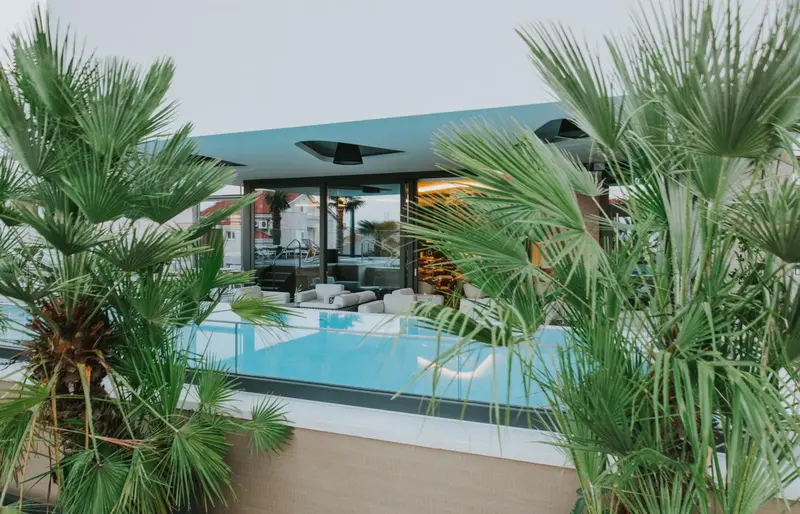 Piscine rectangulaire turquoise bordée de chaises longues blanches et de palmiers.