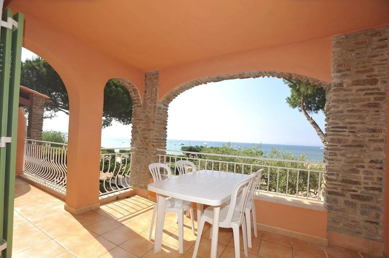Une table et des chaises blanches sont disposées sur une terrasse ombragée avec vue sur la mer.