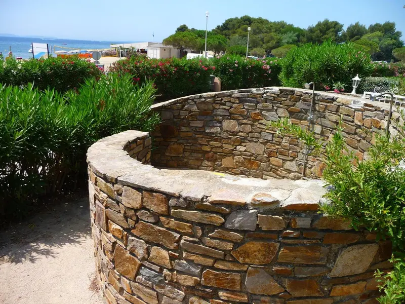 Un muret de pierres entoure un espace fleuri avec une végétation luxuriante.