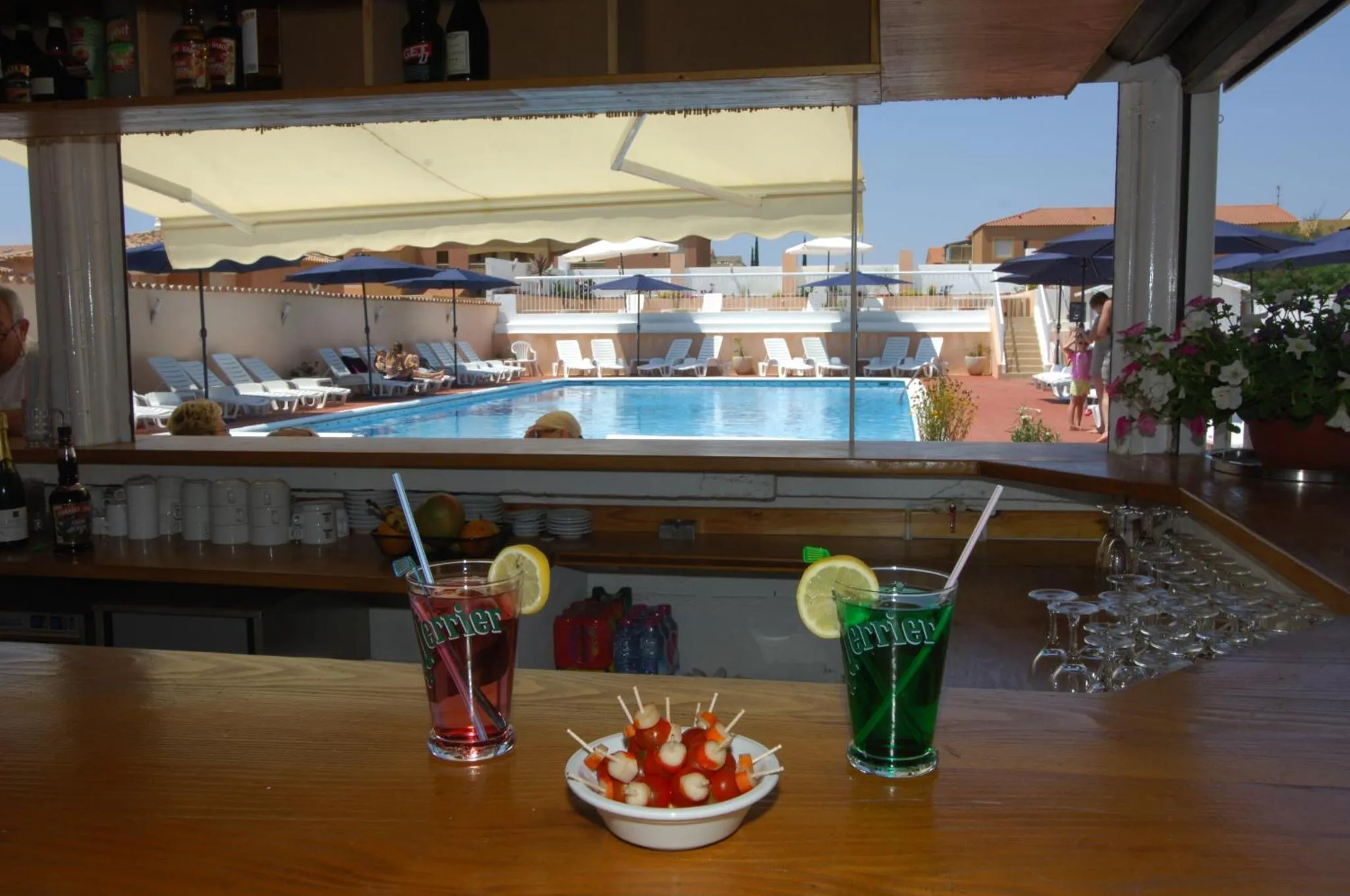 Un comptoir de bar avec des boissons colorées et une vue sur une piscine et des transats.