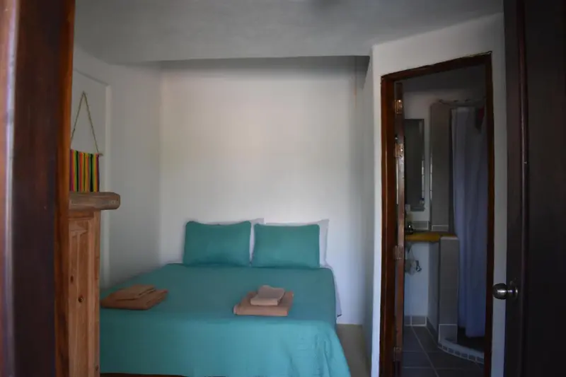 Une chambre avec un lit turquoise et un accès à une salle de bain.