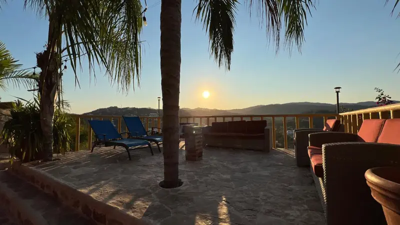 Terrasse avec mobilier de détente et vue sur un paysage montagneux au coucher du soleil.