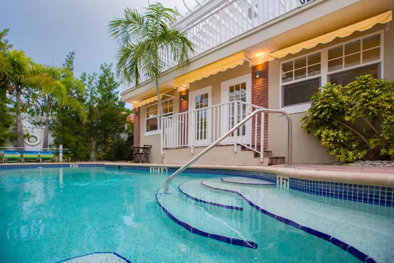 Une piscine turquoise avec des marches et une végétation luxuriante en arrière-plan.