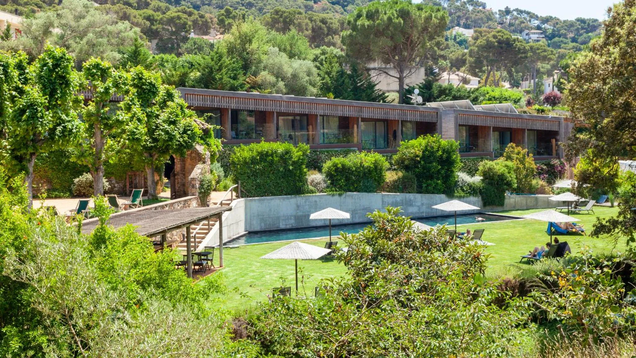 Bâtiment moderne entouré de végétation avec une piscine et des transats.