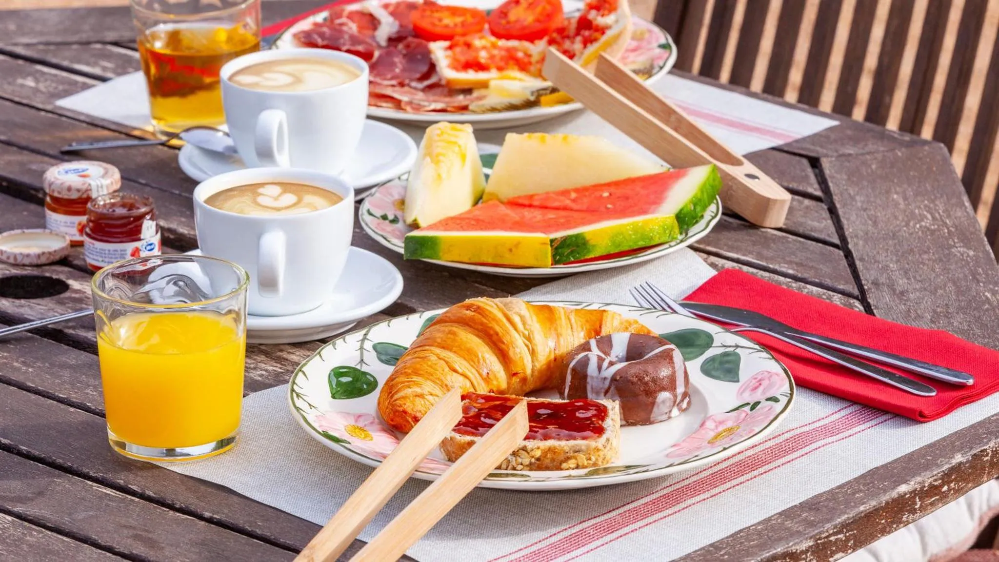 Une table en bois présente un petit-déjeuner avec des viennoiseries, des fruits et des boissons.