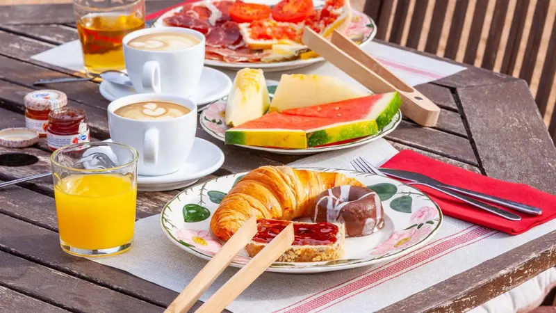 Une table en bois présente un petit-déjeuner avec des viennoiseries, des fruits et des boissons.